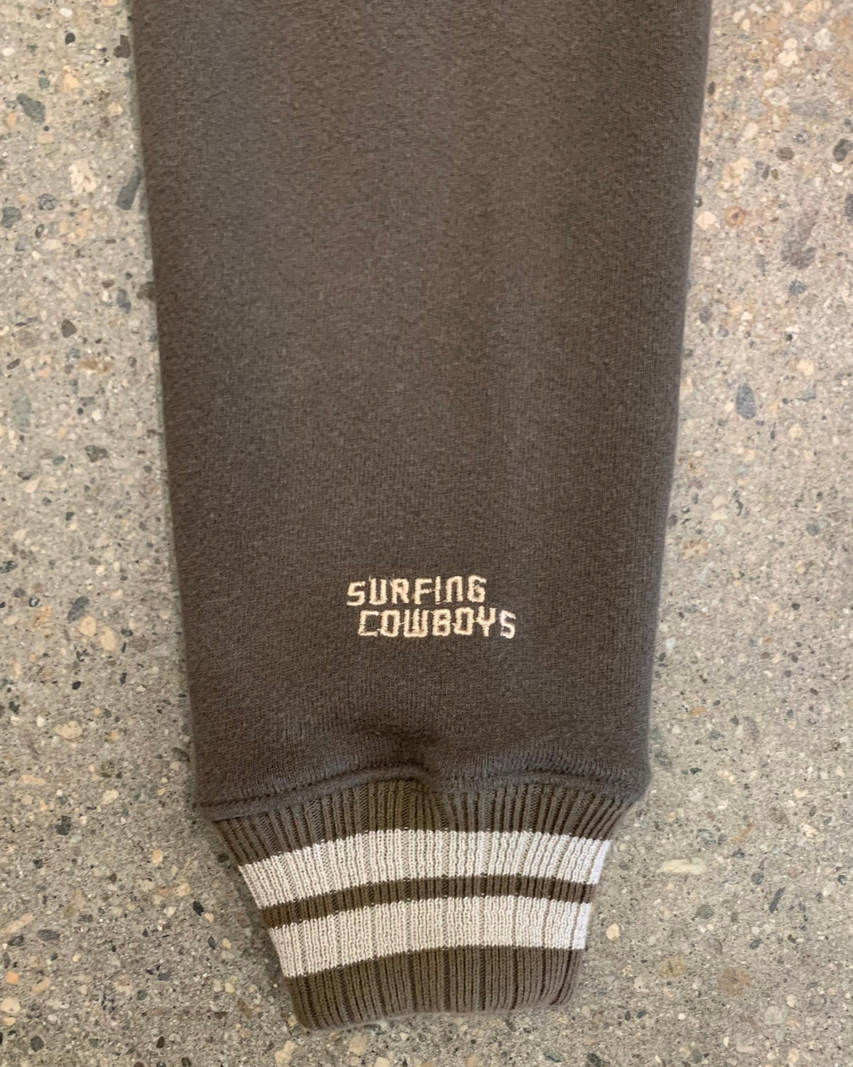Close-up view of the striped cream and brown ribbed cuff featuring white Surfing Cowboys branding embroidered cleanly above the hem.
