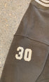 Close-up view of the striped cream and brown ribbed neckline and matching cream applique number 30 stitched on the sleeve.
