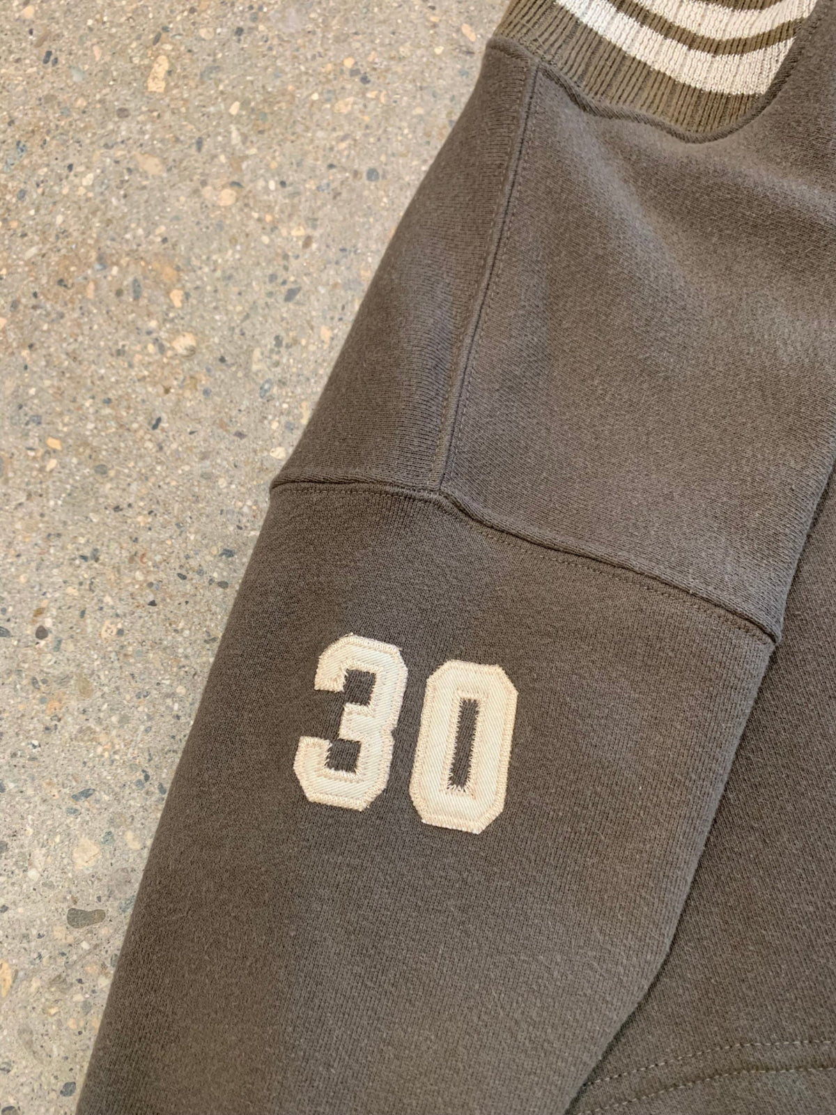 Close-up view of the striped cream and brown ribbed neckline and matching cream applique number 30 stitched on the sleeve.
