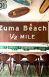 Oversized vintage Zuma Beach metal road sign displayed on wall above dining table, Malibu surf decor vibe.