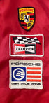 Close-up of Porsche crest, Champion, and USA ’71 Le Mans patches on vintage racing jacket.
