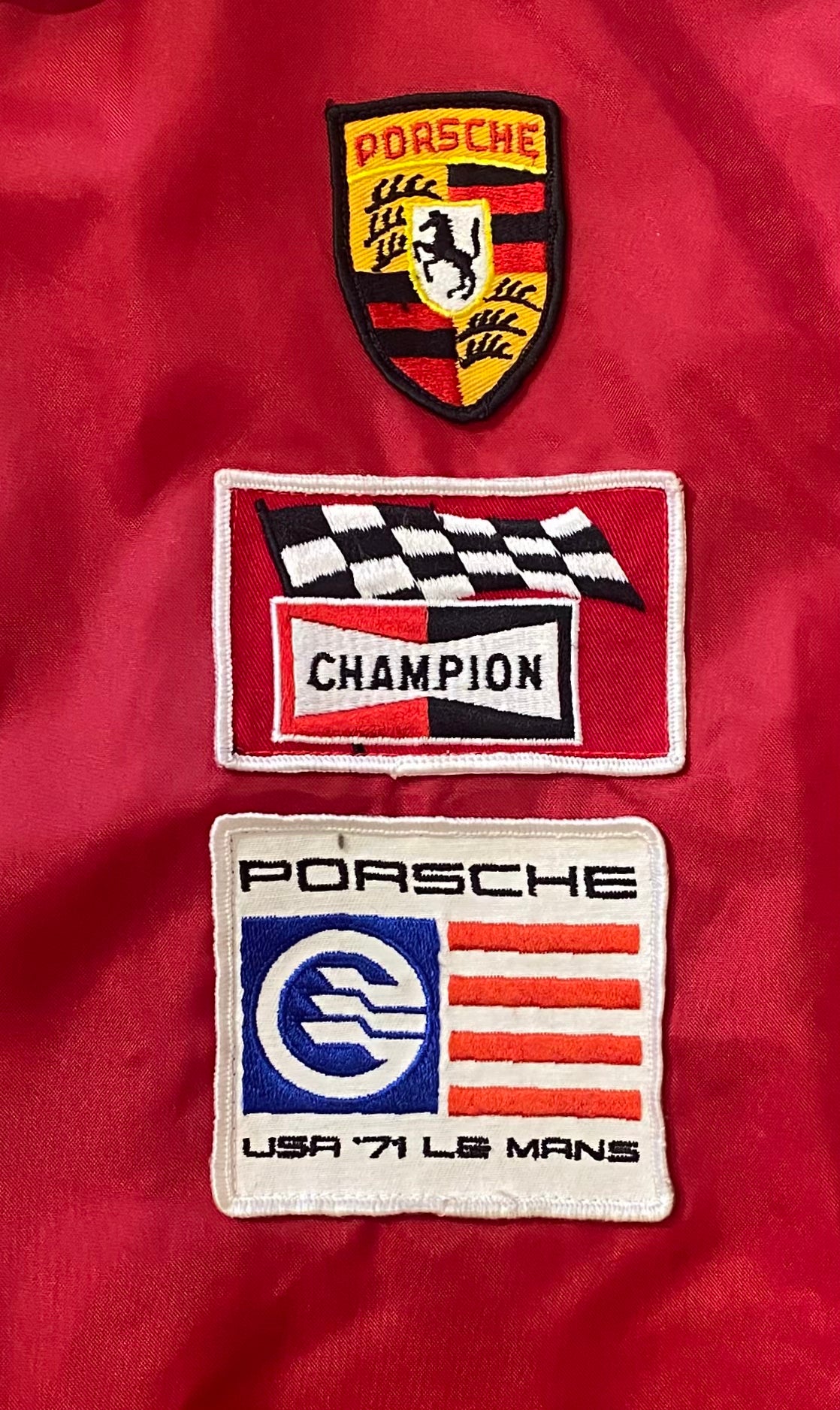 Close-up of Porsche crest, Champion, and USA ’71 Le Mans patches on vintage racing jacket.
