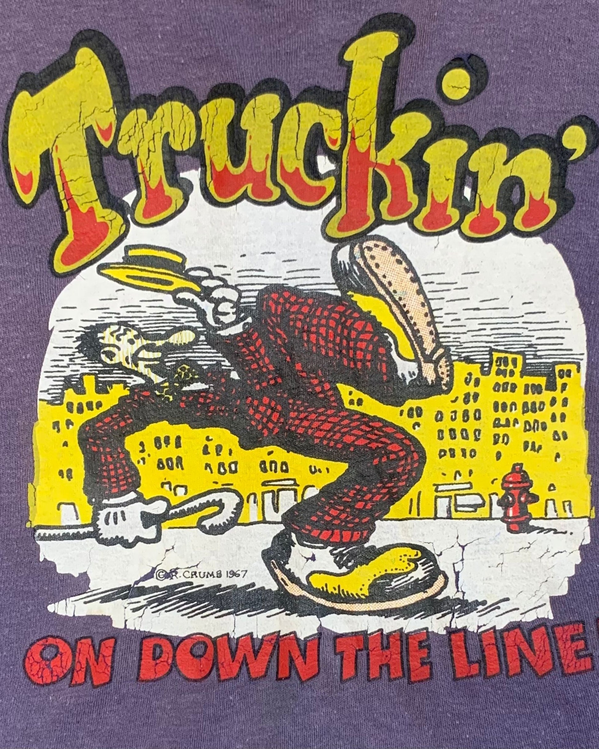 Close-up of the front graphic on a purple tank top with yellow “Truckin’” lettering, a walking cartoon figure, and red “On Down the Line” text.