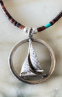 Close-up of sterling sailboat pendant in round frame, showing sculptural detail and patina.