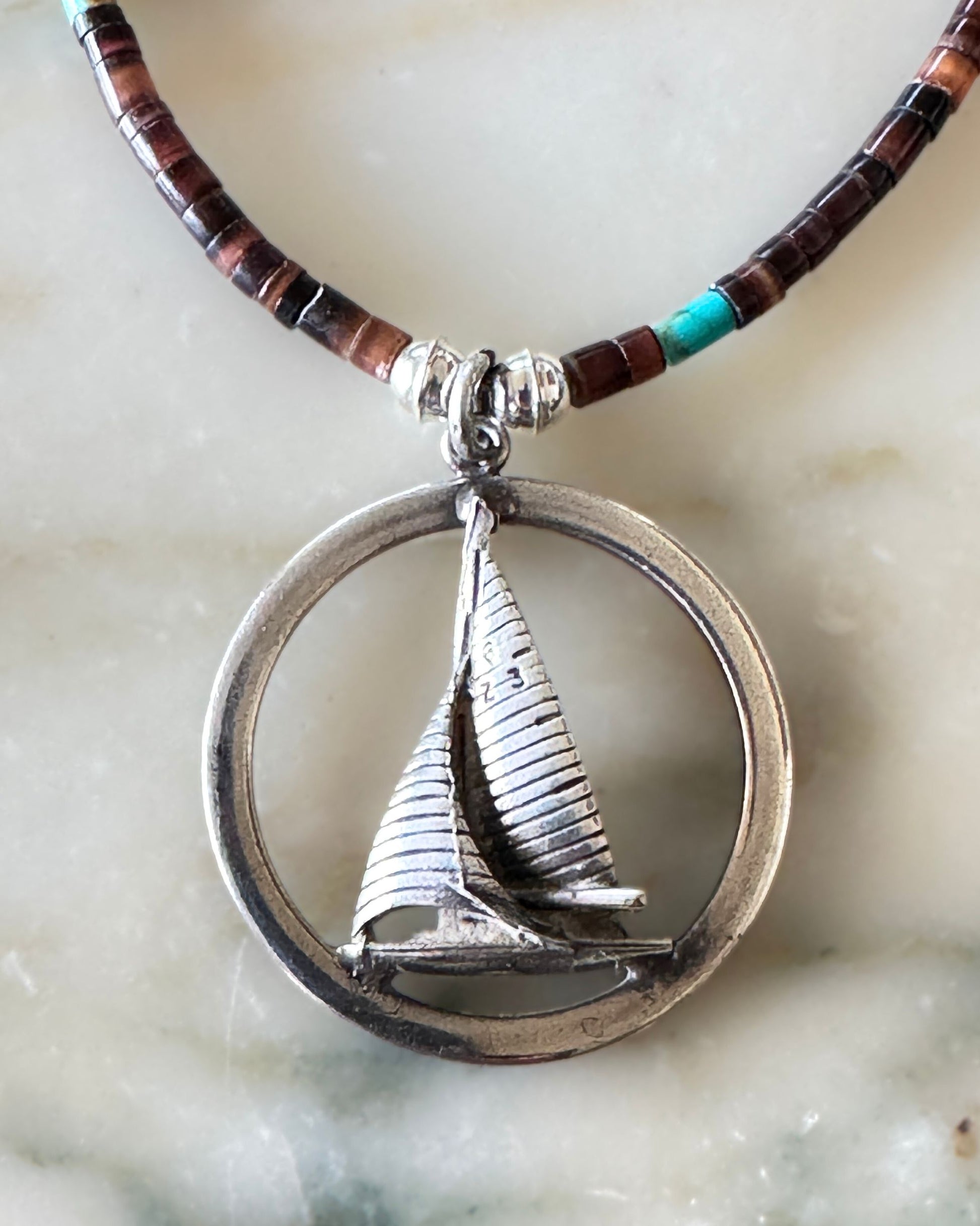 Close-up of sterling sailboat pendant in round frame, showing sculptural detail and patina.
