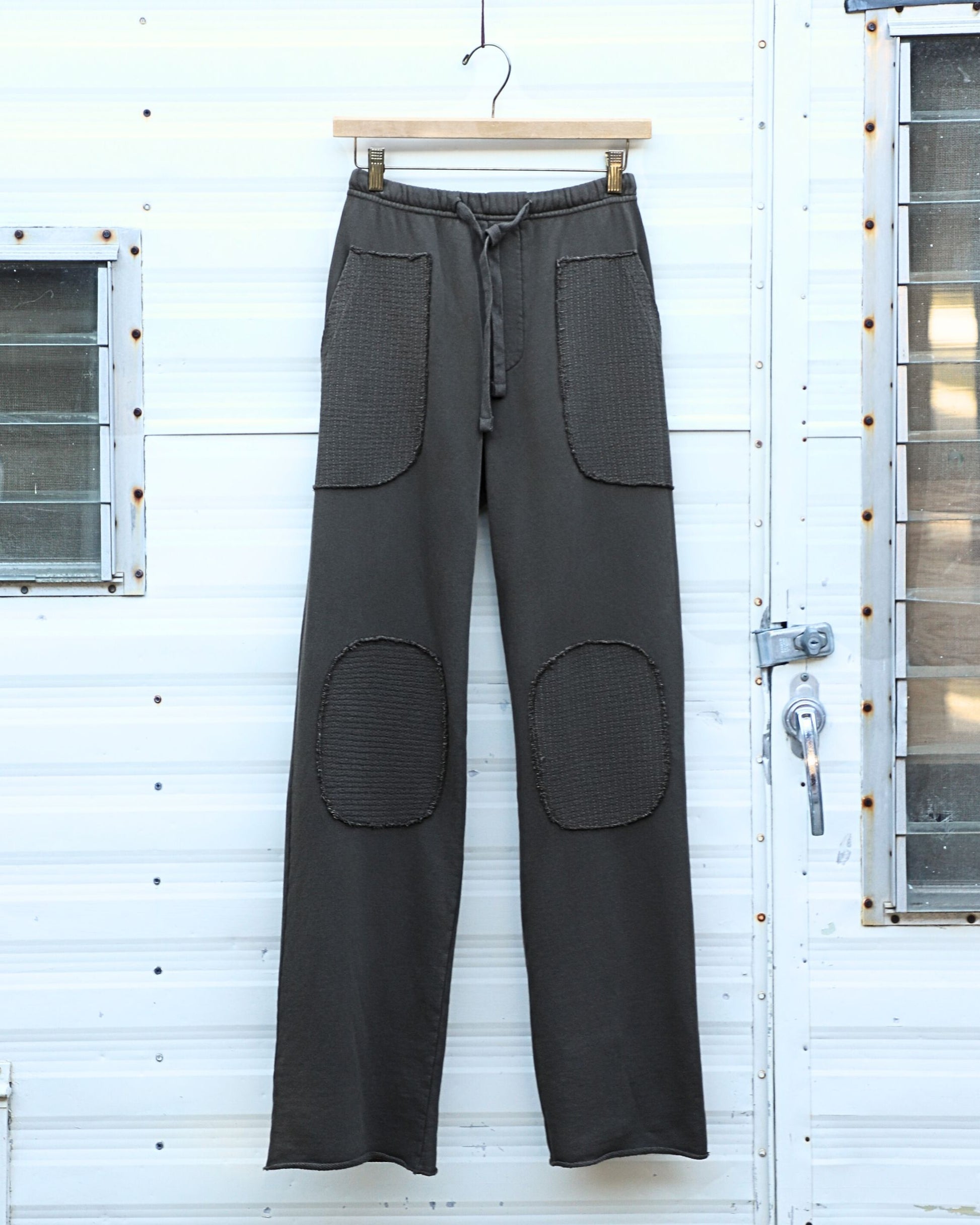 Front-on view of mocha patch pants hanging on a wood hanger.