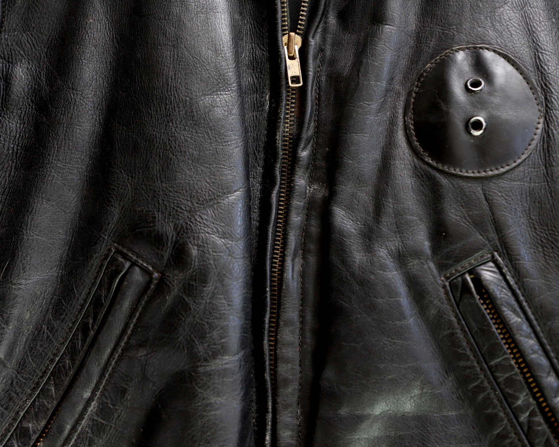 Details of zipper and leather patch 1950s Taubers black horsehide leather jacket with lace-up sides, Western-inspired yoke, and visible signs of wear.
