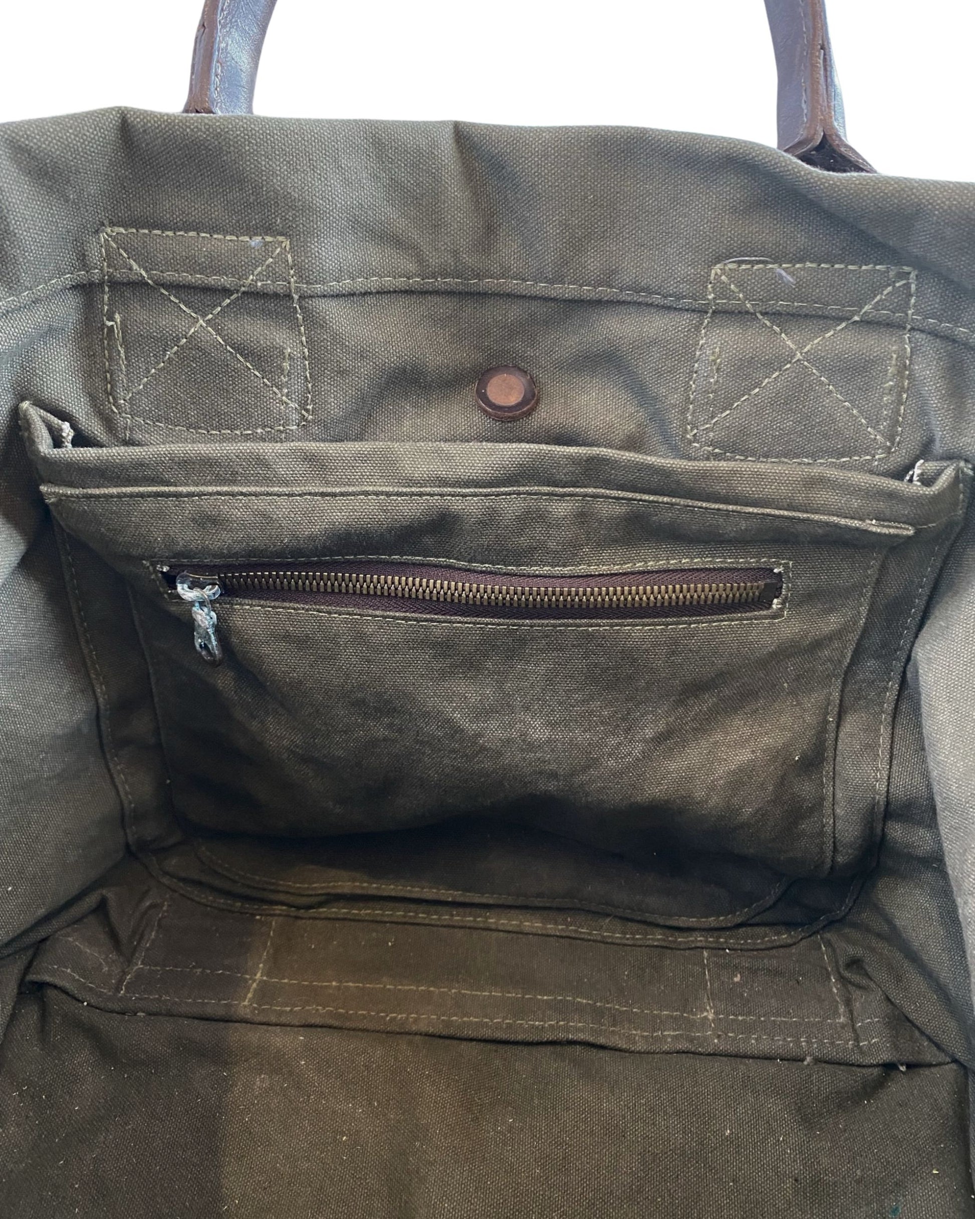 Vintage olive green canvas military tote with brown leather handles and webbing straps, interior zip pocket shown. Inside Detail.