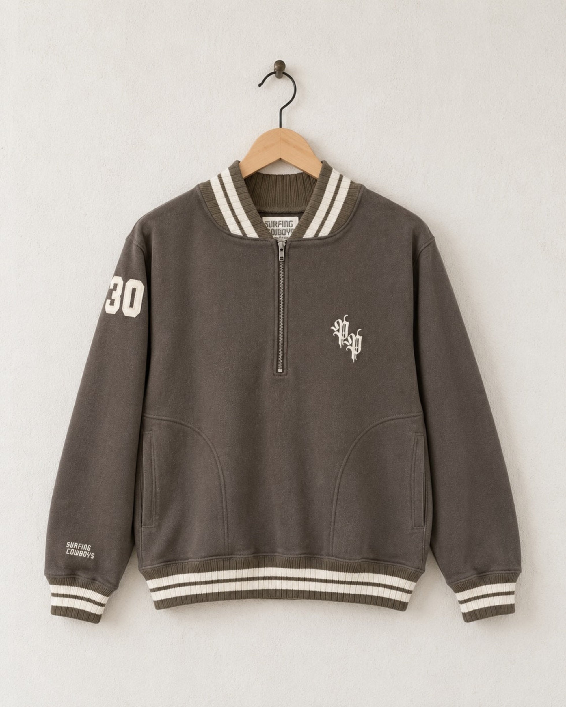 Front view of a mocha brown 100% cotton half-zip neighborhood sweatshirt with cream striped varsity ribbing, front pockets, an Old Californio-inspired chest monogram, and a felt 30 shoulder patch.