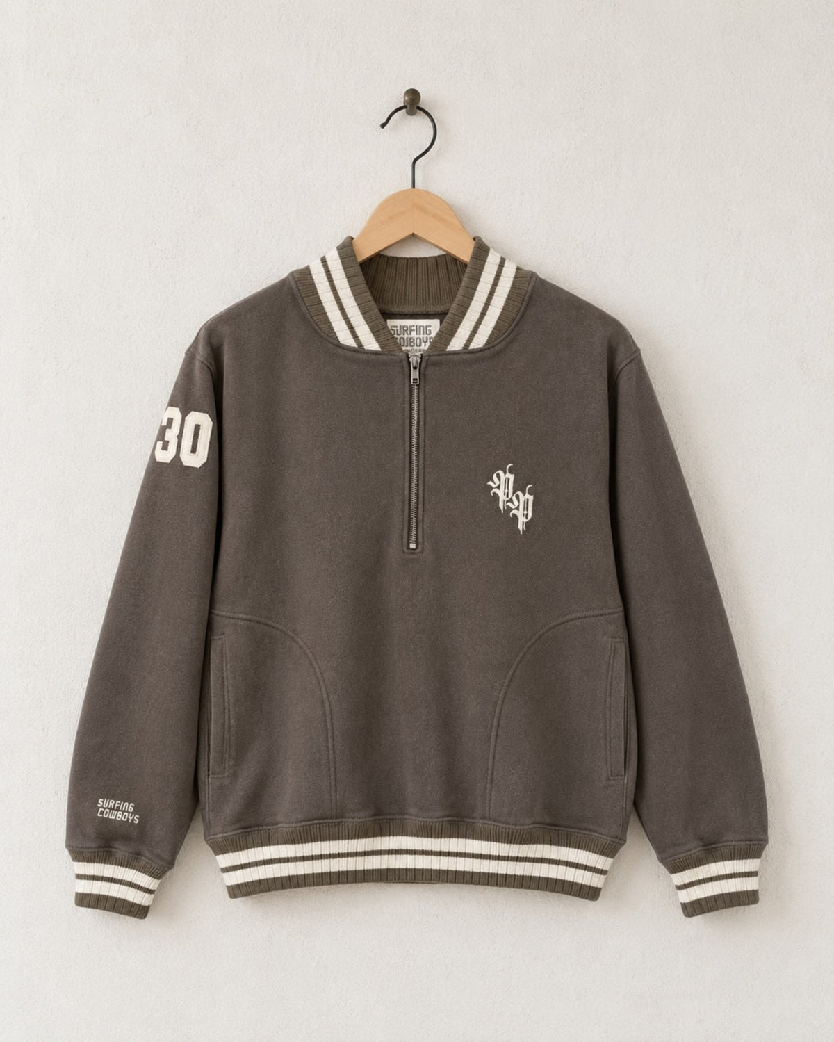 Front view of a mocha brown 100% cotton half-zip neighborhood sweatshirt with cream striped varsity ribbing, front pockets, an Old Californio-inspired chest monogram, and a felt 30 shoulder patch.