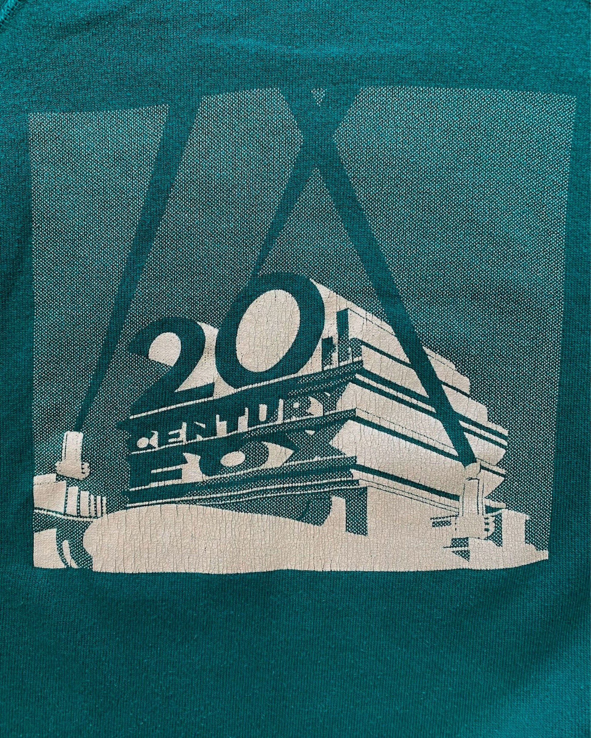 Close-up of 20th Century Fox halftone screen print graphic on green sweatshirt showing aged ink crazing and studio monument logo detail.