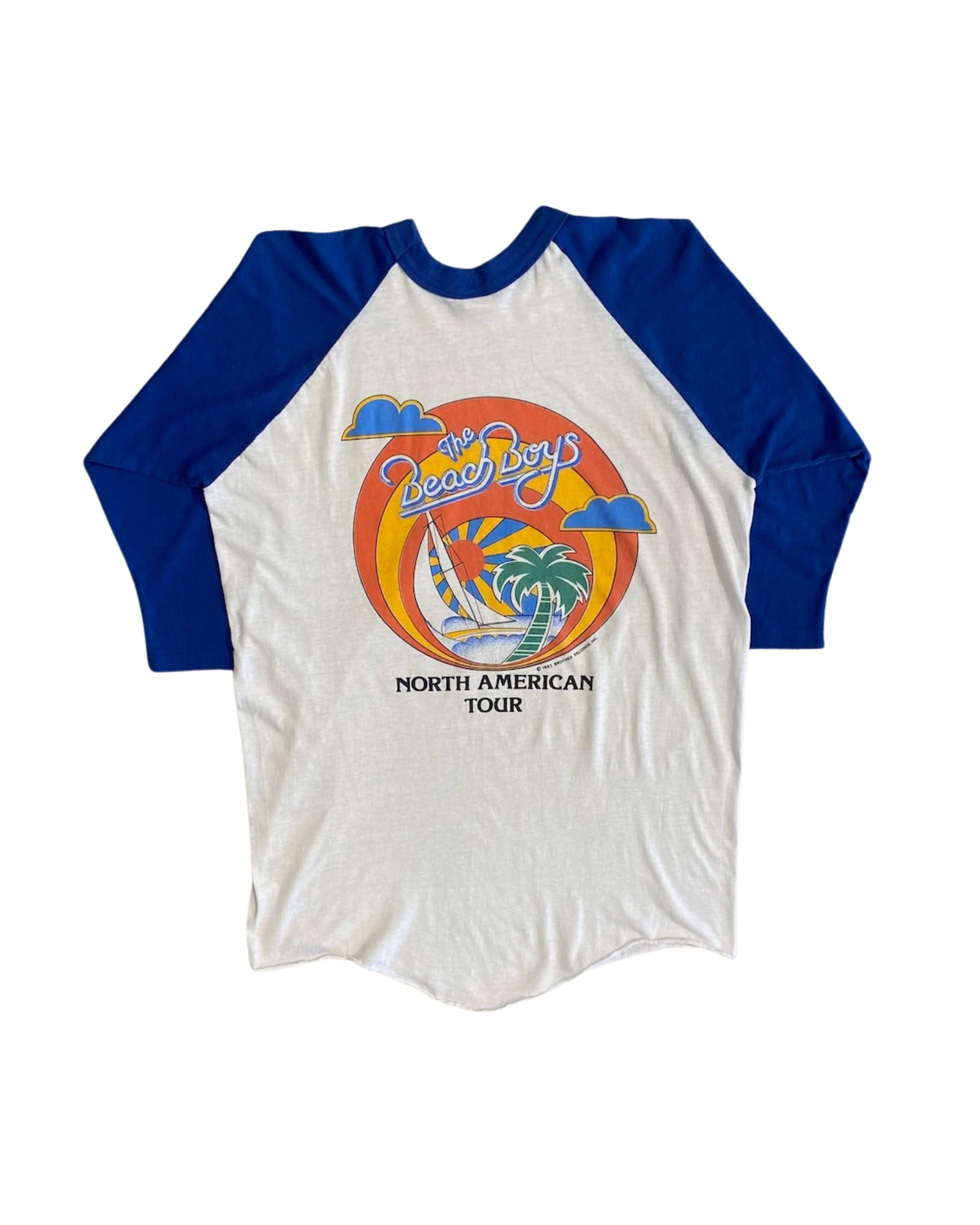 Back view of 1982 Beach Boys North American Tour raglan tee showing full circular sunset graphic with sailboat and palm tree, on white background.