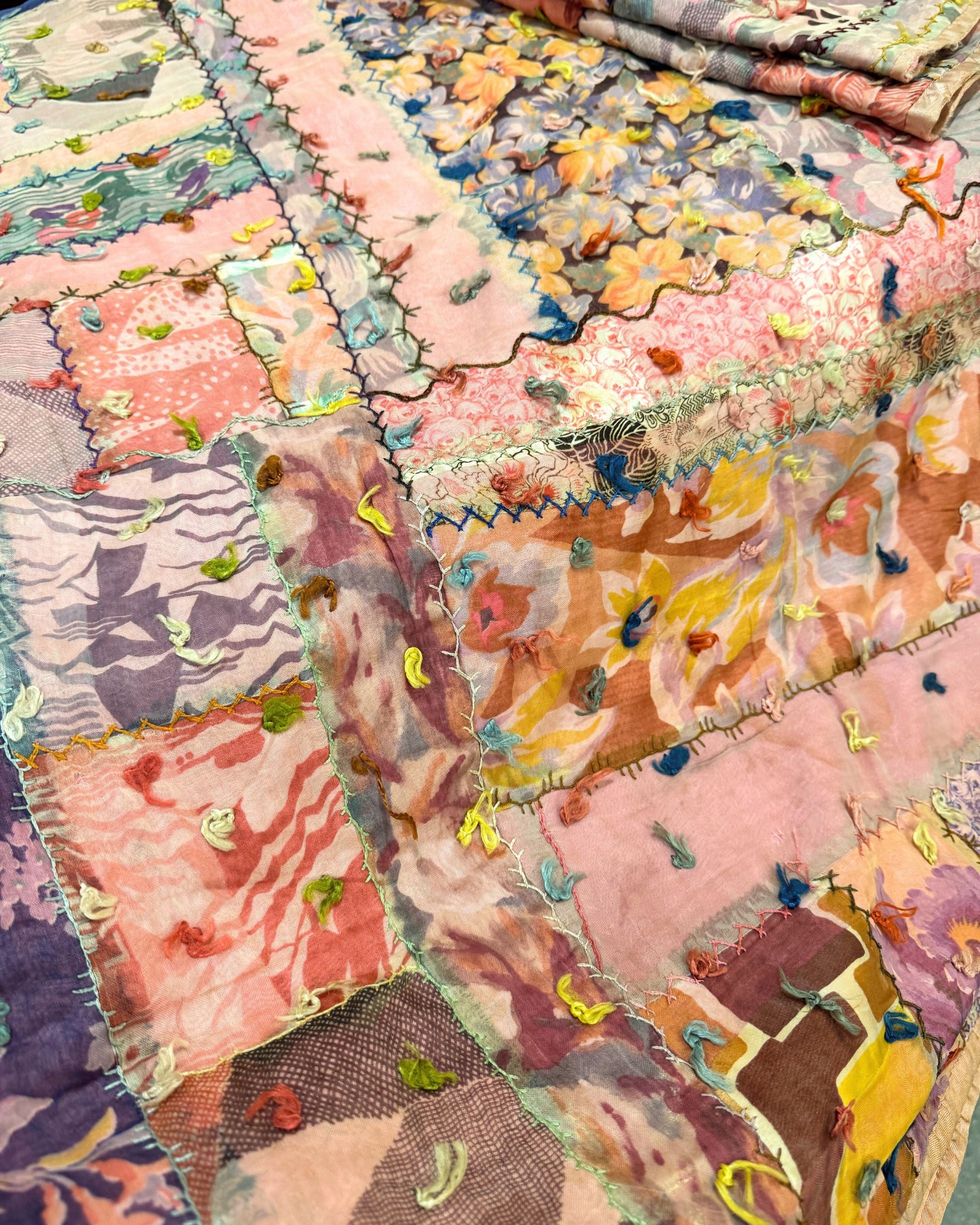 Close-up of vintage silk patchwork quilt with colorful embroidery.
Detail of chenille-tufted fabric patches on mid-century textile.
