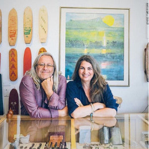 Two people sitting at a table with surfboards and a painting on the wall.