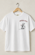 Front view of vintage white Surfing Cowboys Wicked Good pocket T-shirt with front devil graphic on hanger against tan wall. 