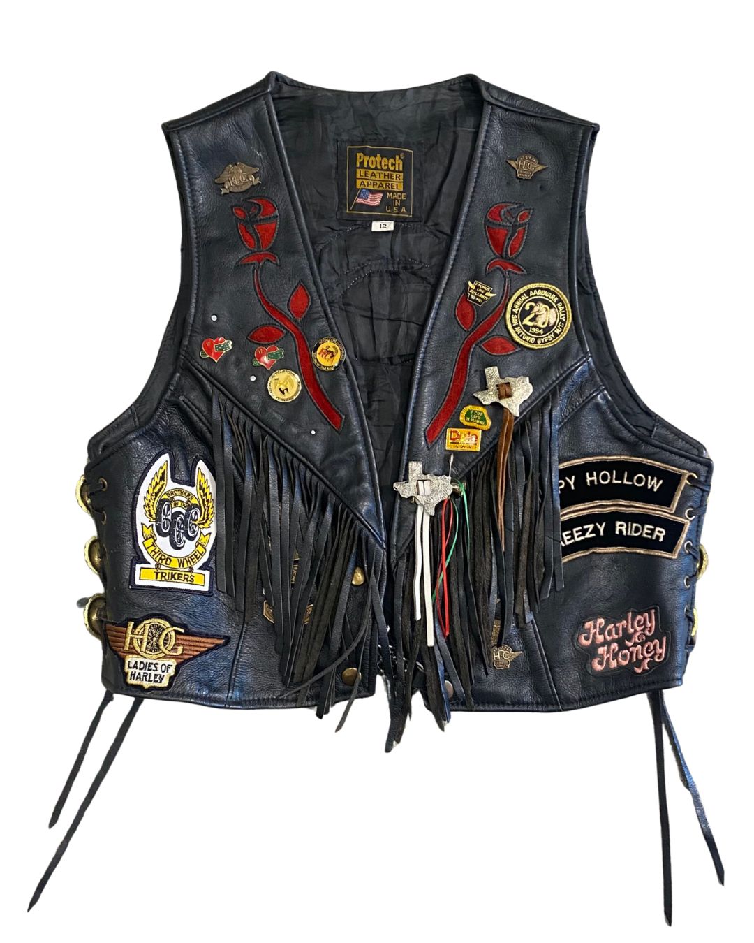 Wide shot of full front of 1980s Harley Davidson leather vest, showing patches, fringe, and pins.with fringe and H.O.G. patches.