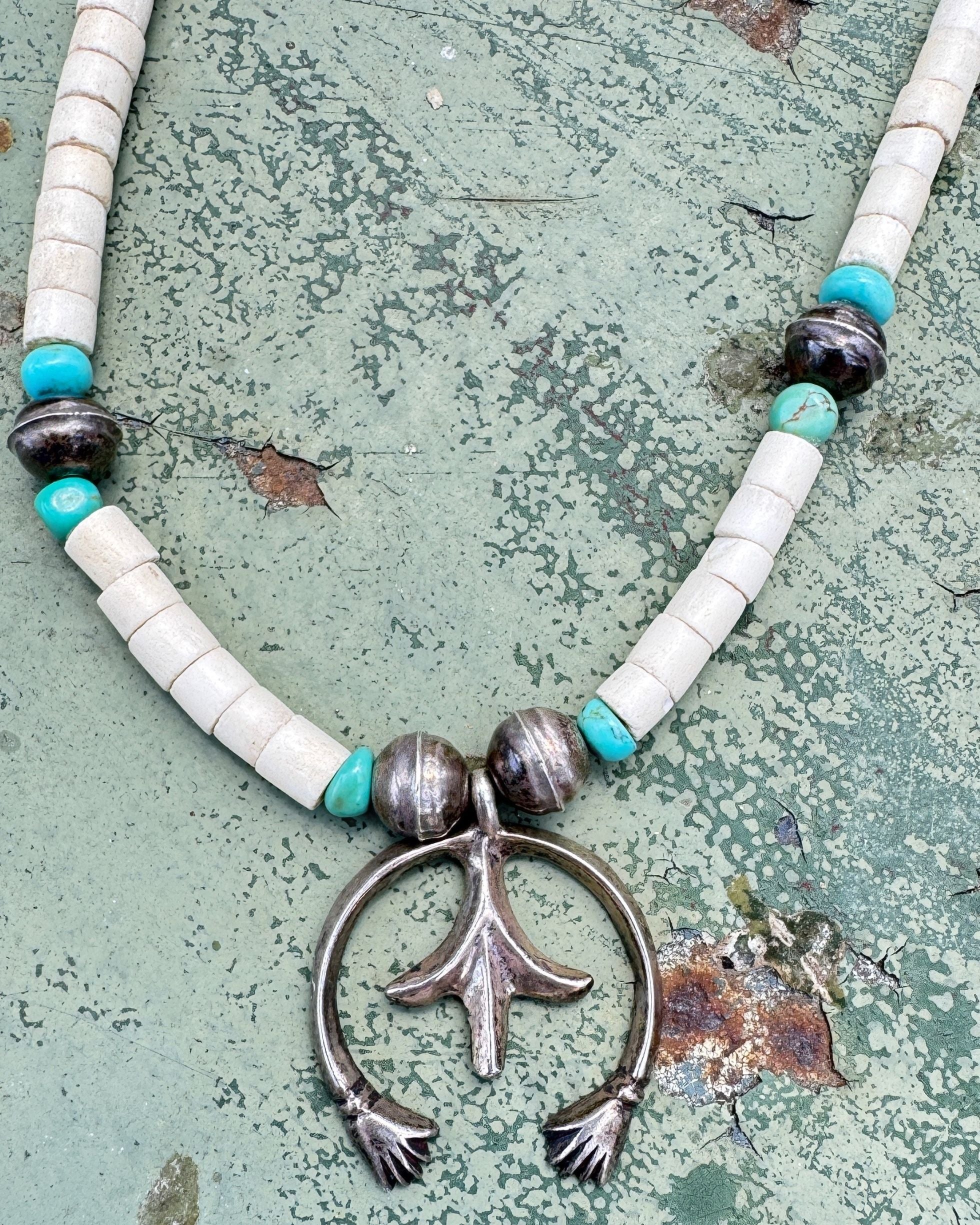 Close-up of vintage sterling silver naja-style pendant with turquoise and white beads.
