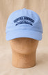 Front view of Surfing Cowboys Rising Sun Cap in light blue with navy embroidered crest on a wooden display head.