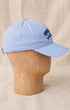 Side view of light blue Surfing Cowboys Rising Sun Cap showing curved bill, navy embroidered crest, and adjustable back strap.