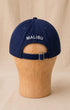 Back view of navy Surfing Cowboys Rising Sun Cap with creamy-white MALIBU embroidery and adjustable buckle strap.