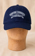 Front view of Surfing Cowboys Rising Sun Cap in navy with creamy-white embroidered crest on a wooden display head.