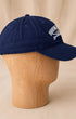 Side view of navy Surfing Cowboys Rising Sun Cap showing curved bill, embroidered crest, and adjustable back strap.