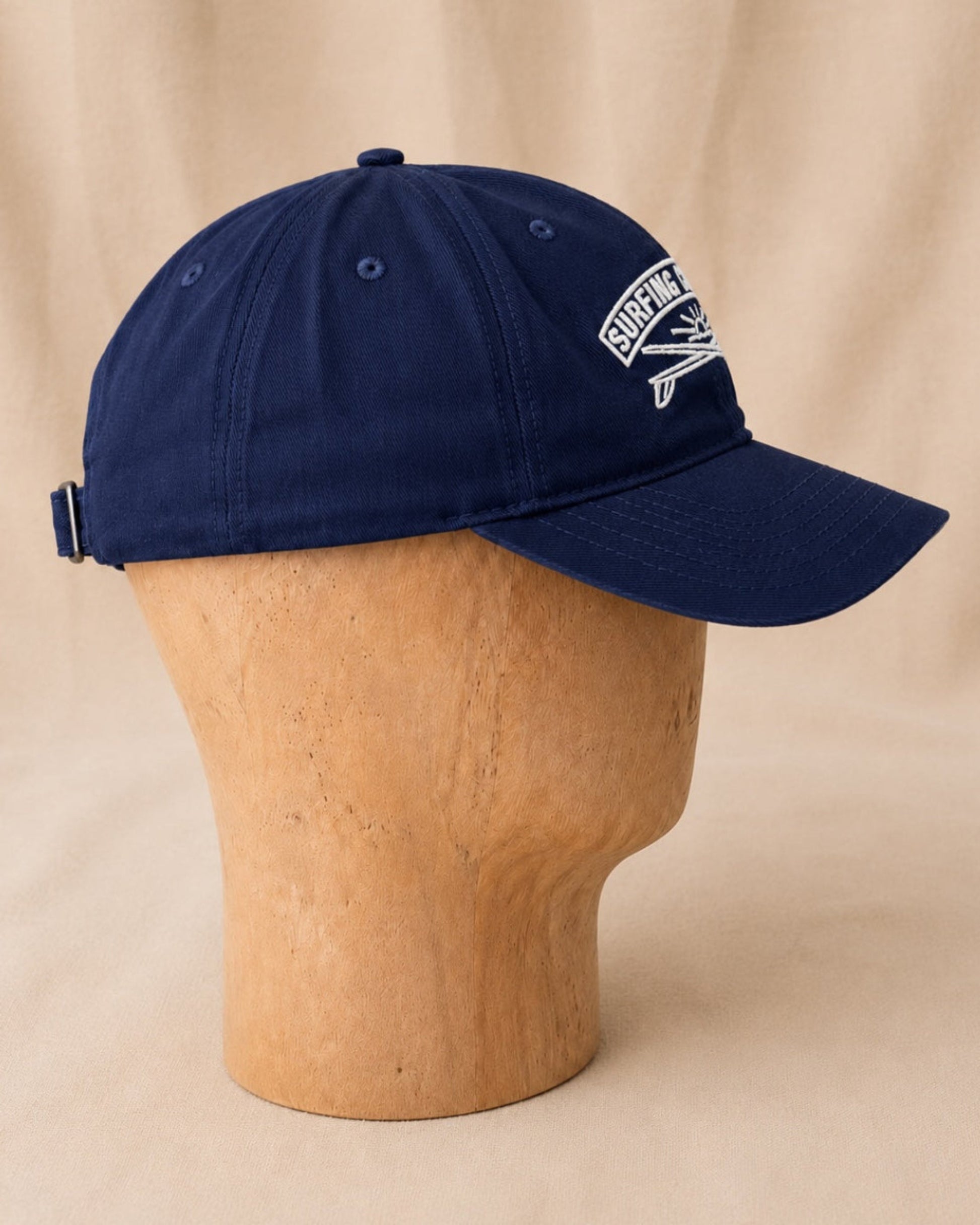Side view of navy Surfing Cowboys Rising Sun Cap showing curved bill, embroidered crest, and adjustable back strap.