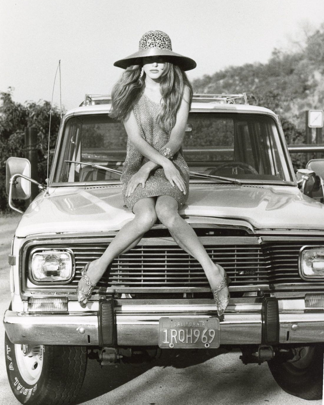 Black & White Photo Of Woman Sitting On Jeep With Dress And Hat